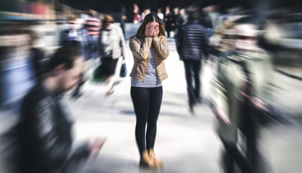 Woman standing in the middle of a busy area with hands over her face and the background blurred