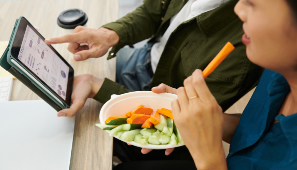 Woman eating a slice of carrot from a bowl with veggies at an office