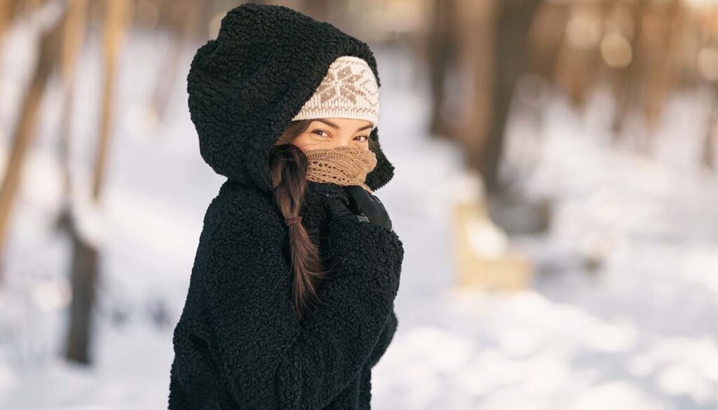 woman protecting her skin in cold temperatures with snowy backdrop 