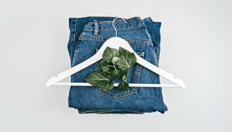 Leaves on top of white hanger on top of folded blue jeans