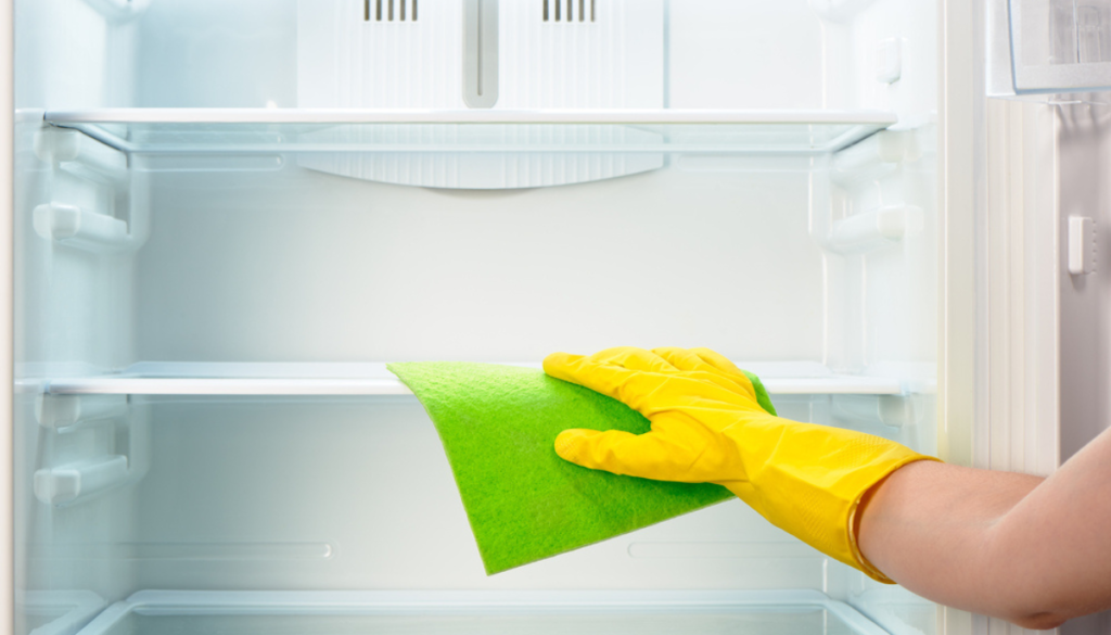 Hand in yellow rubber glove using green cloth to clean empty fridge