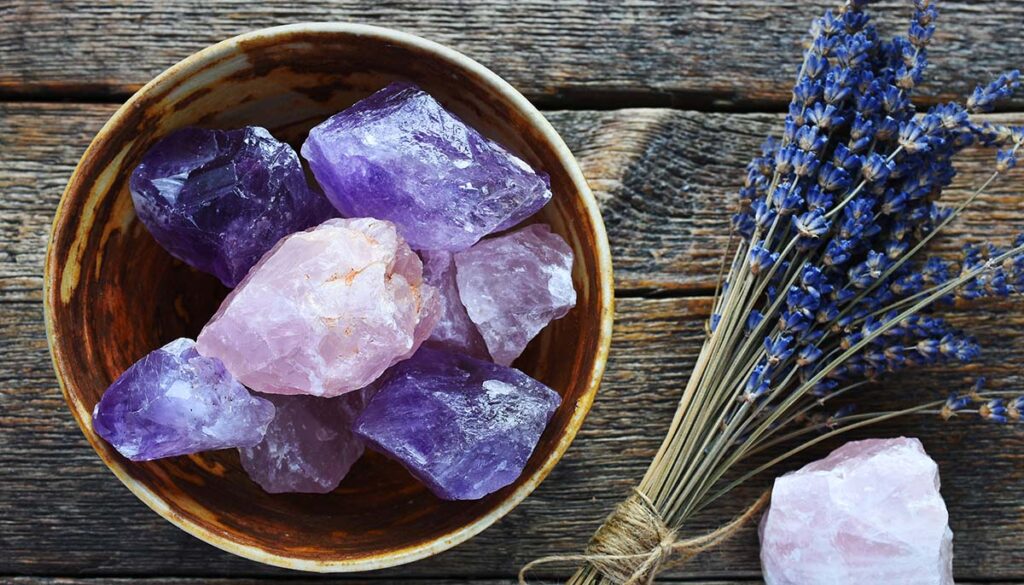 A table top image of a pottery bowl with large rose quartz and amethyst crystal with dried lavender flowers.