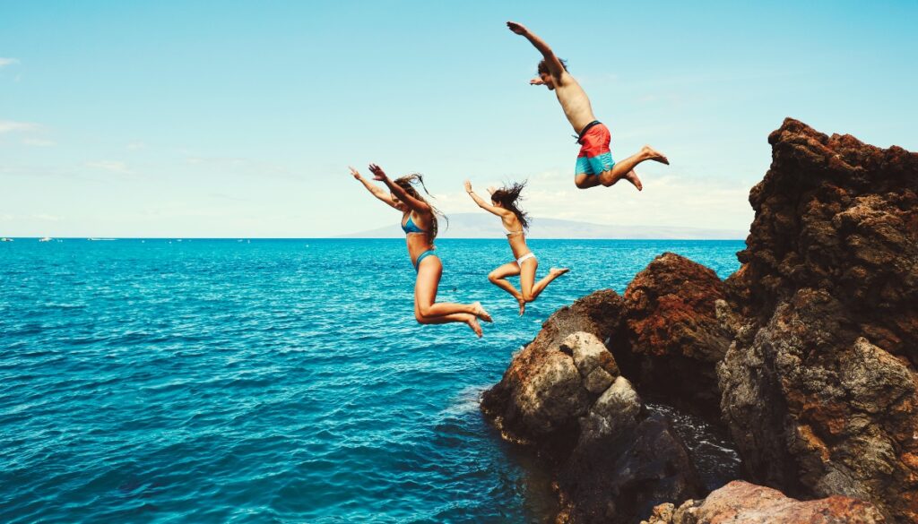 friends jumping off of a rock into water