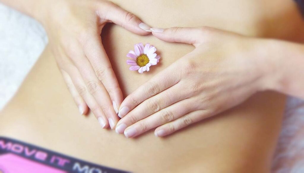 woman making heart with hands over stomach with flower in belly button