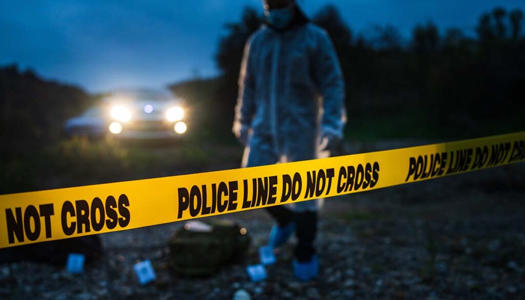 Forensic police investigator collecting evidence at the crime scene by the river in nature at night selective focus on police line tape