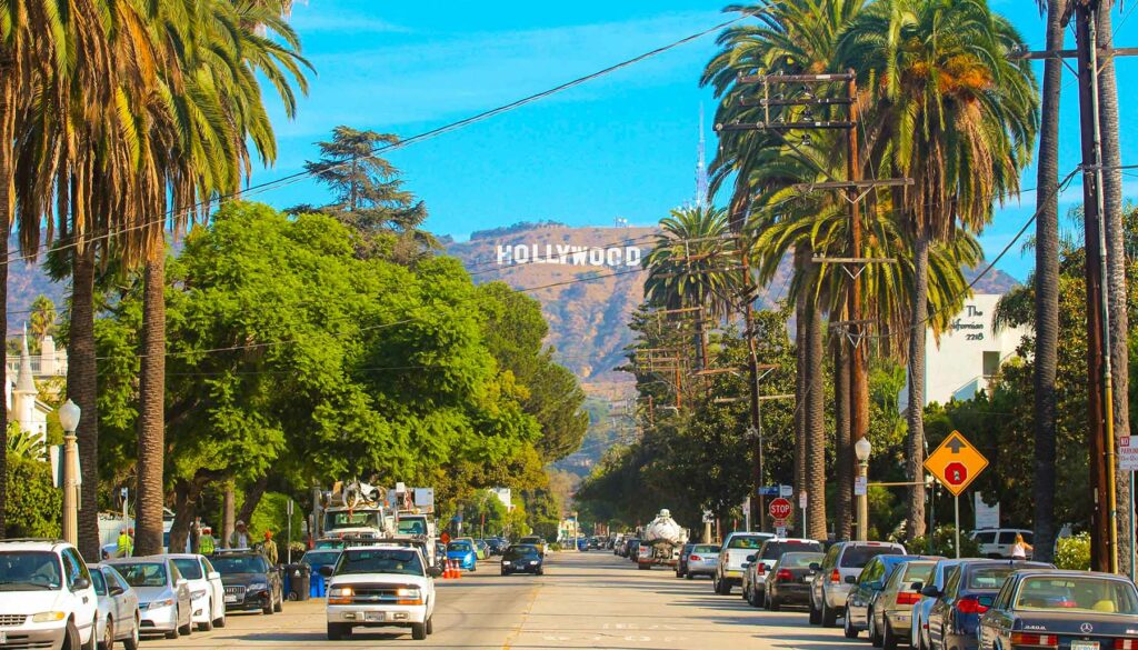 Hollywood sign district in Los Angeles, USA. Beautiful Hollywood highway road with cars, palms and a sign on the hills. Clear blue sky.