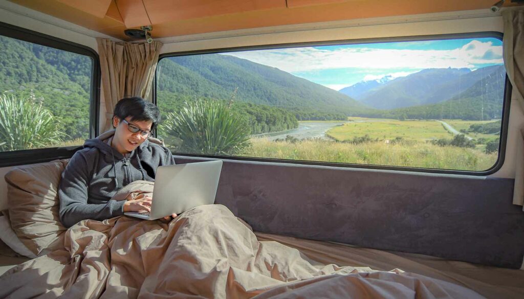 man working on laptop from great outdoors in tent or camper