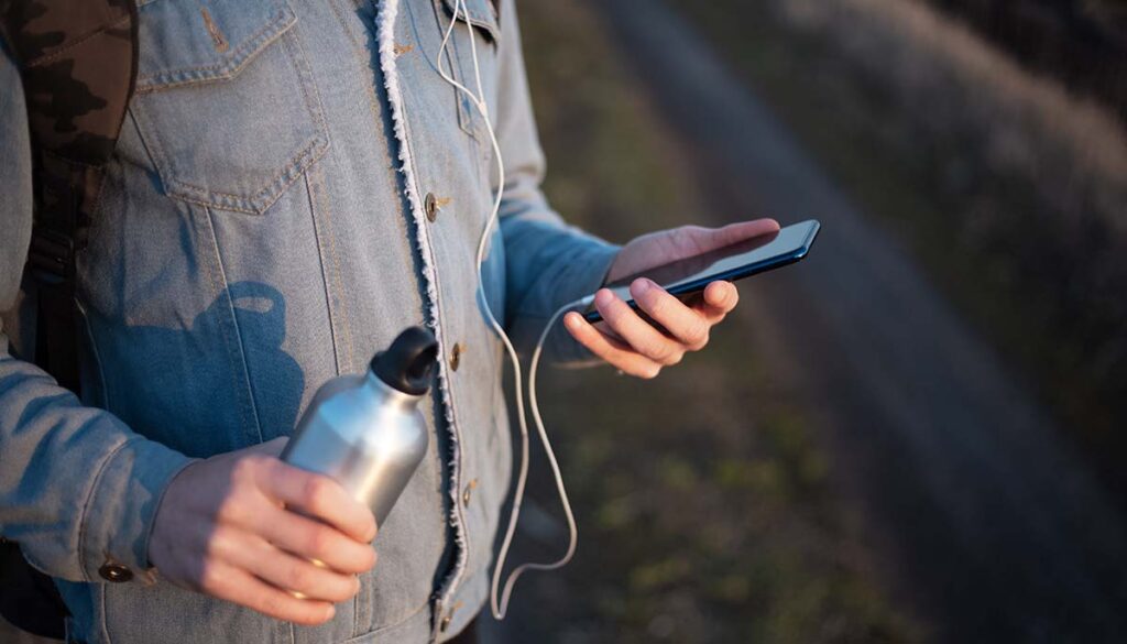 outside looking at phone holding a stainless steel reusable water bottle