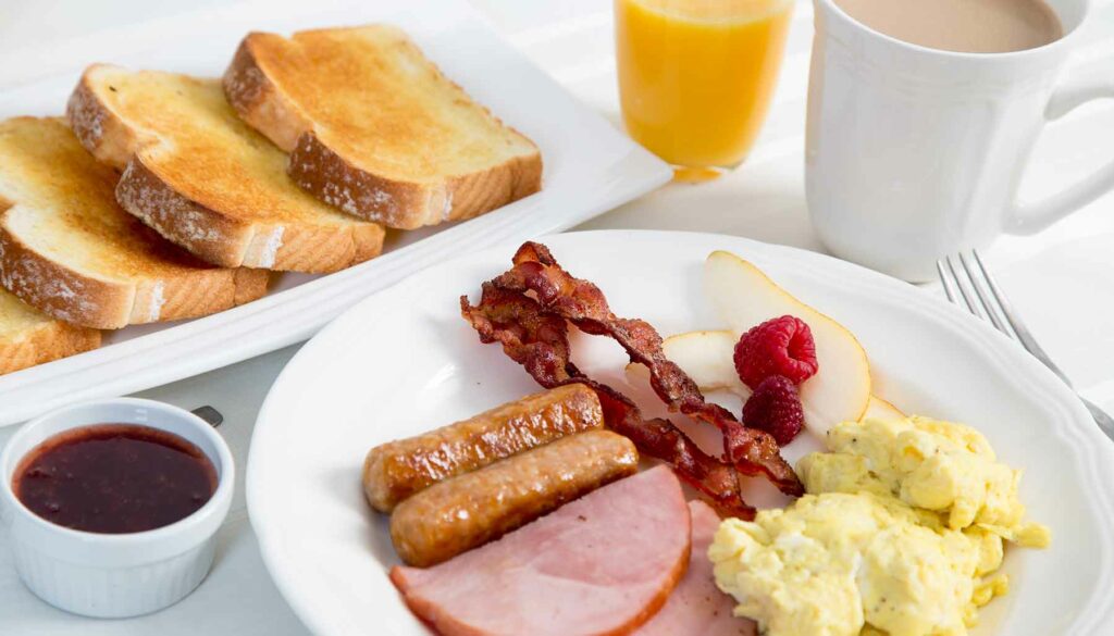 American breakfast with toast, bacon, sausage, hame, eggs, coffee, orange juice