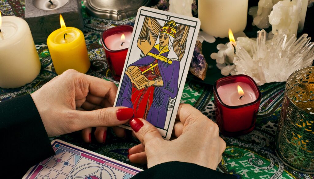 two hands holding a high priestess card surrounded by candles