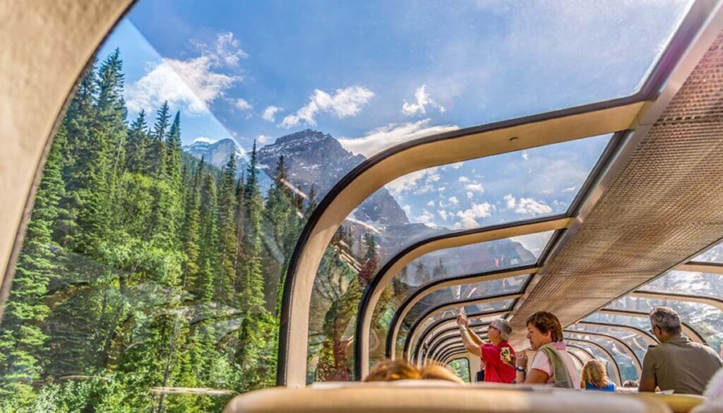 Rocky Mountaineer passing through Vancouver on a sunny day with forest and mountains through the glass ceiling