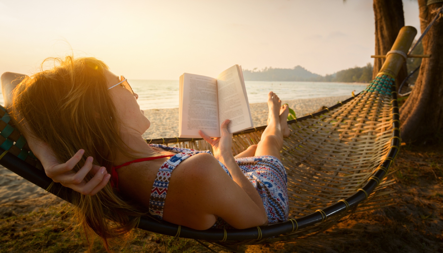 woman reading on a beach in a hammock